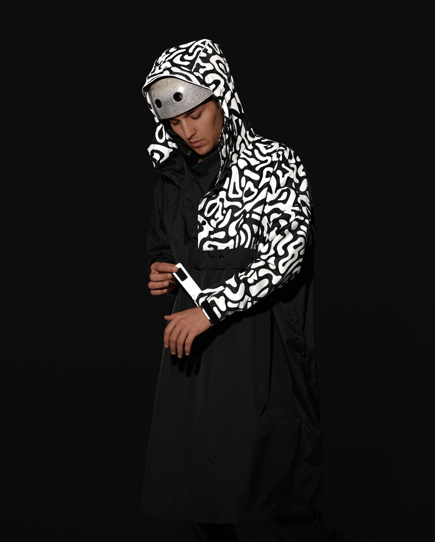 Poncho imperméable noir avec motifs réfléchissants, porté de nuit en ville par un cycliste.