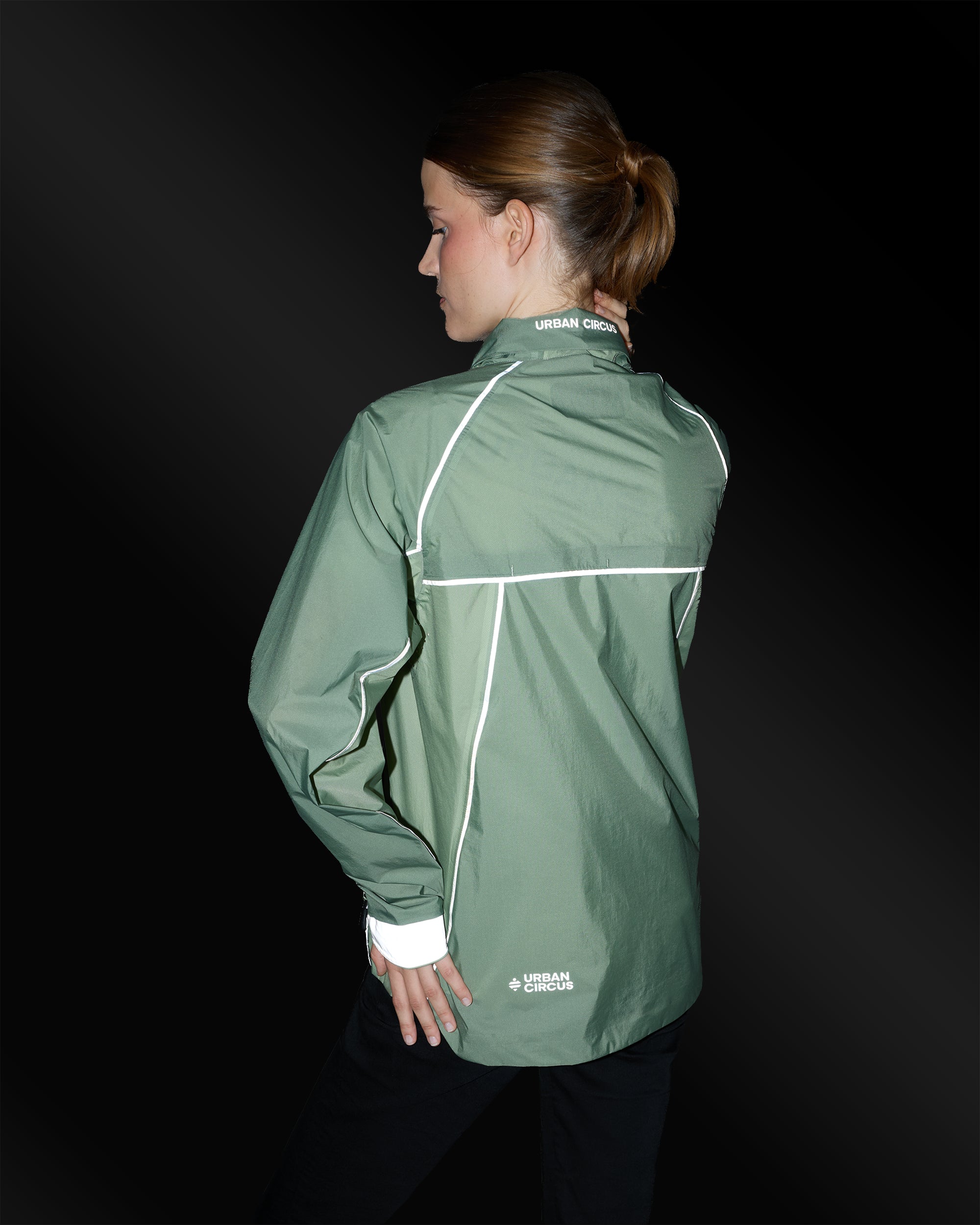 Kompakte, ultraleichte Jacke in Salbeigrün mit reflektierenden Details an einer Frau bei Nacht von hinten